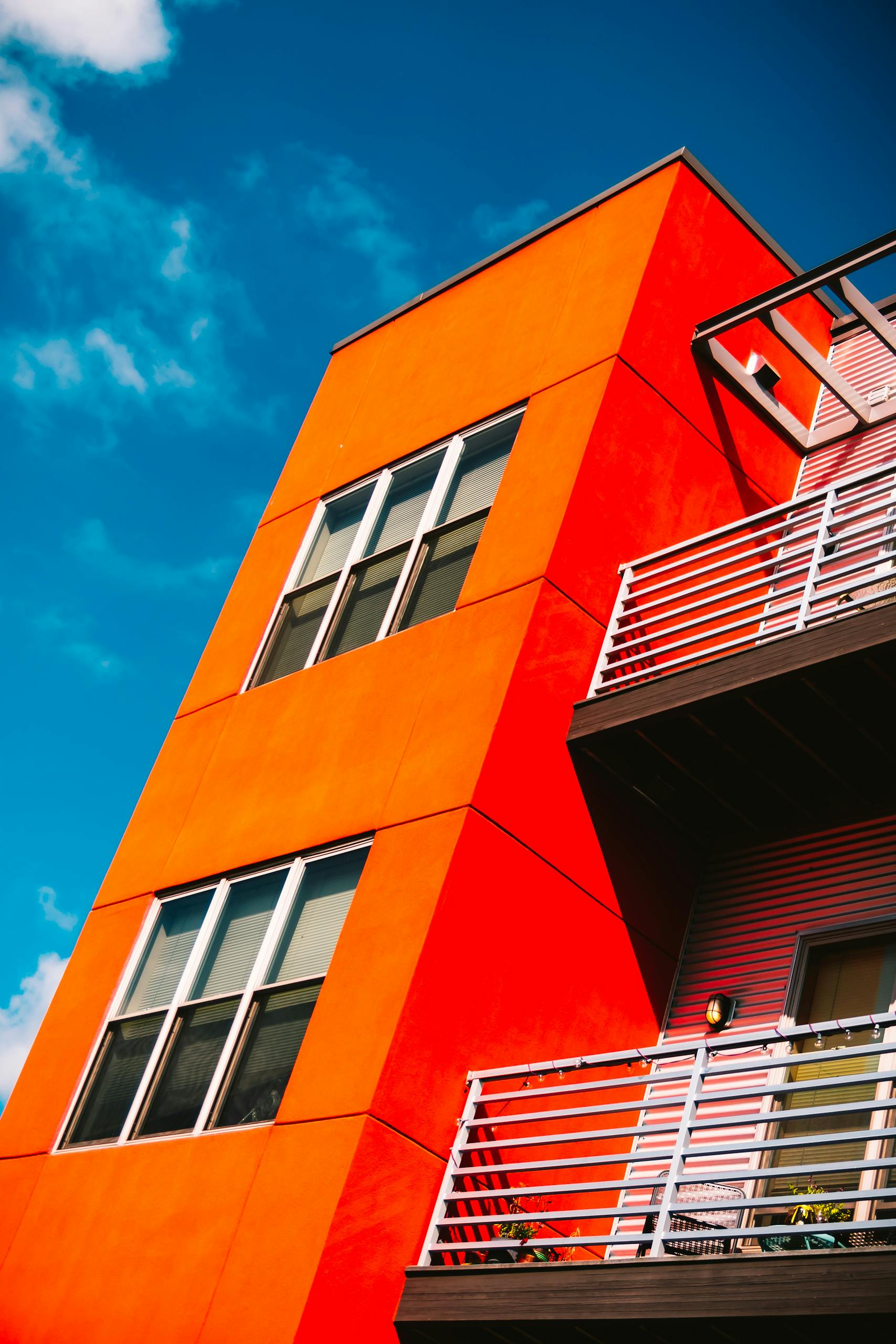 Low angle of a vibrant orange modern apartment building against a bright blue sky in Eau Claire.